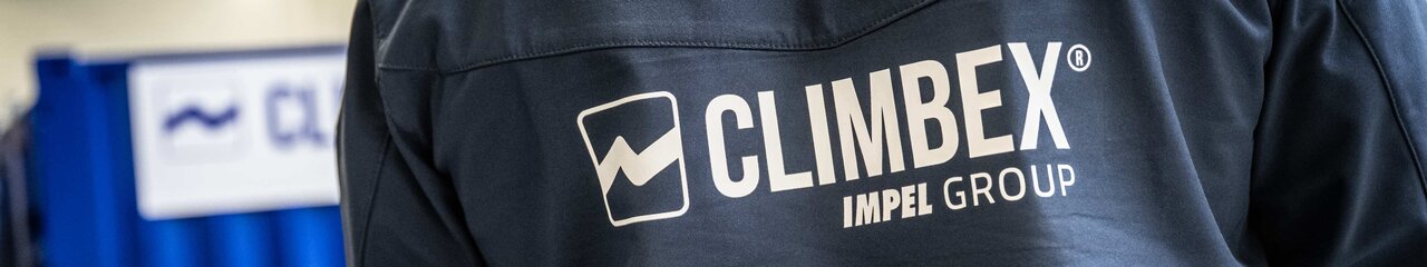 Aufnahme eines Rückens eines Climbex Mitarbeiter, welcher eine dunkelblaue Arbeiter-Jacke trägt auf der das Climbex Logos mit dem Zusatz 'Impel Group' Schriftzug zu sehen ist. Im Hintergrund sind unscharf ein Gerät und Climbex-Container zu sehen.
