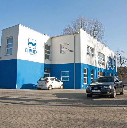 Gezeigt wird das Climbex Polen Gebäude von außen, links an der Wand ist riesig das Climbex-Logo zu und davor stehen verschiedene Autos.