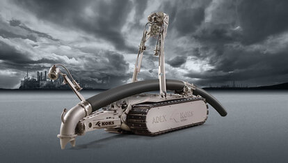 Roboter mit Schlauch, der Richtung Boden zeigt, und Kameras, zur Steuerung durch einen Mitarbeiter. Im Hintergrund ist weit in der Ferne Industrie-Landschaft zu sehen, zusammen mit dunkelgrauen Wolken und Boden.