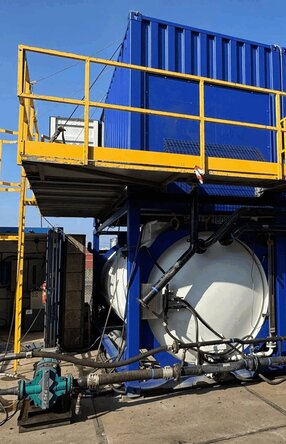 Zu sehen ist eine Konstruktion auf einem Gelände, bestehend aus drei großen weißen Tanks auf denen jeweils ein königsblauer Container steht in dem vermutlich die Motoren und Rohre sind.