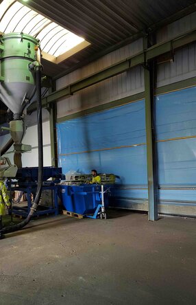 Zu sehen ist eine Halle mit einer relativ großen Siebanlage die von einem Mitarbeiter in neongelber Arbeitskleidung und Schutzhelm bedient wird.